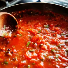 Sos pomidorowy z ziołami na patelni, idealny do spaghetti ze słoika. Drewniana łyżka miesza gorący sos.