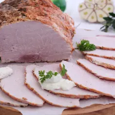 Pyszna pieczona szynka w rękawie, pokrojona w plastry, z dodatkiem chrzanu i natki pietruszki.