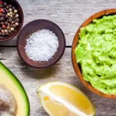Czy guacamole jest zdrowe? Na drewnianym blacie leży połówka awokado, miseczki z solą i pieprzem, cytryna i gotowe guacamole.