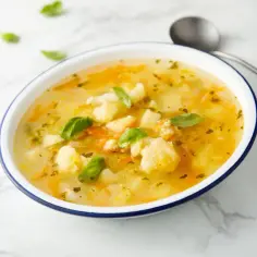 Aksamitna zupa kalafiorowa z kawałkami warzyw i listkami bazylii. Idealna na szybki obiad, gdy zastanawiasz się, ile gotuje się kalafior w zupie.