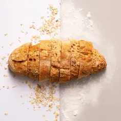 Chleb krojony, posypany płatkami owsianymi i mąką grubo mieloną.