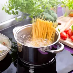 Gotujesz spaghetti? Sprawdź, ile makaronu na porcję, by nikt nie był głodny. Na kuchence wrze woda, a obok czekają świeże warzywa.