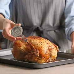Sprawdzanie temperatury kurczaka w środku za pomocą termometru. Złocisty, pieczony drób na tacy.