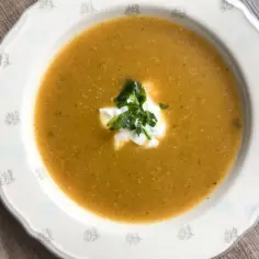 Aksamitna zupa na bazie rosołu, udekorowana kleksem śmietany i świeżą natką pietruszki, podana w ozdobnej miseczce.
