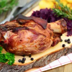 Pieczona golonka z chrupiącą skórką, podana z czerwoną kapustą i ziemniakami. Idealne jakie przyprawy do golonki? Zioła i pieprz.