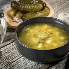 Miseczka zupy ogórkowej, obok ogórki kiszone i czosnek. Zastanawiasz się, ile może stać zupa ogórkowa?