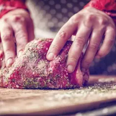 Ręce nacierają surowe mięso dziczyzny ziołami i solą. Idealne przyprawy do dziczyzny podkreślą jej smak.