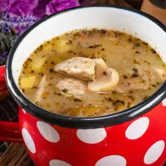 Pyszna zupa grzybowa z kawałkami mięsa i ziemniaków w czerwonym kubku w białe kropki. Zastanawiasz się, ile można trzymać zupę w lodówce?