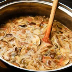 Gotowanie wywaru na zupę grzybową. Drewniana łyżka miesza bulgoczący wywar z kawałkami grzybów w metalowym garnku.