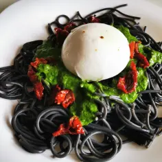 Czarny makaron spaghetti z zielonym pesto, suszonymi pomidorami i kulką mozzarelli. To danie, gdzie "co to jest sepia w makaronie" nabiera nowego znaczenia.