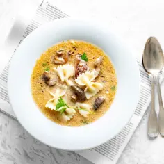Zupa grzybowa z makaronem w kształcie motylków, podana w białej misce. Czy zastanawiasz się, ile kcal ma zupa grzybowa z makaronem?