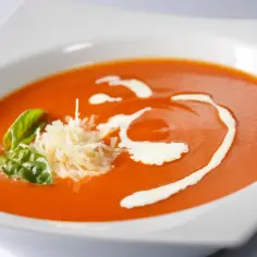 Pomidorowa zupa na diecie, udekorowana bazylią i parmezanem, z delikatną śmietanką. Idealna na lekki posiłek.