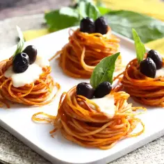 Cztery małe gniazdka spaghetti z oliwkami i bazylią. Idealne, by ustalić, ile gniazdek makaronu na osobę.