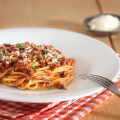 Porcja spaghetti bolognese na białym talerzu, posypana parmezanem. Zastanawiasz się, ile kcal ma spaghetti bolognese?