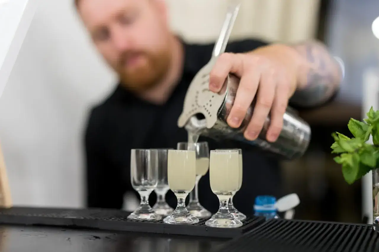 Barman nalewa drinki do kieliszków. Zastanawiasz się, ile kosztuje barman na wesele? Taki profesjonalista zapewni niezapomniane wrażenia.