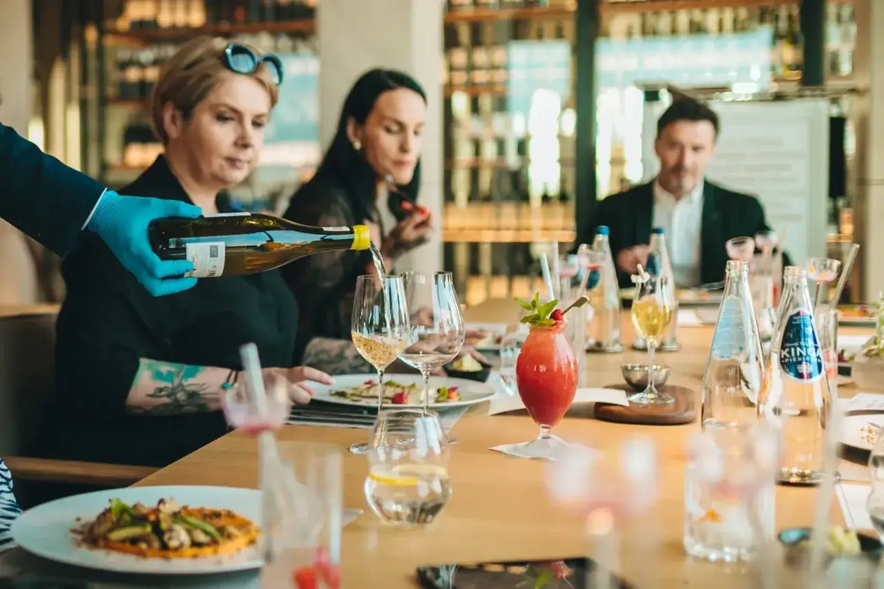 Elegancki lunch w Gdańsku. Kelner nalewa wino, na stole koktajl i dania.