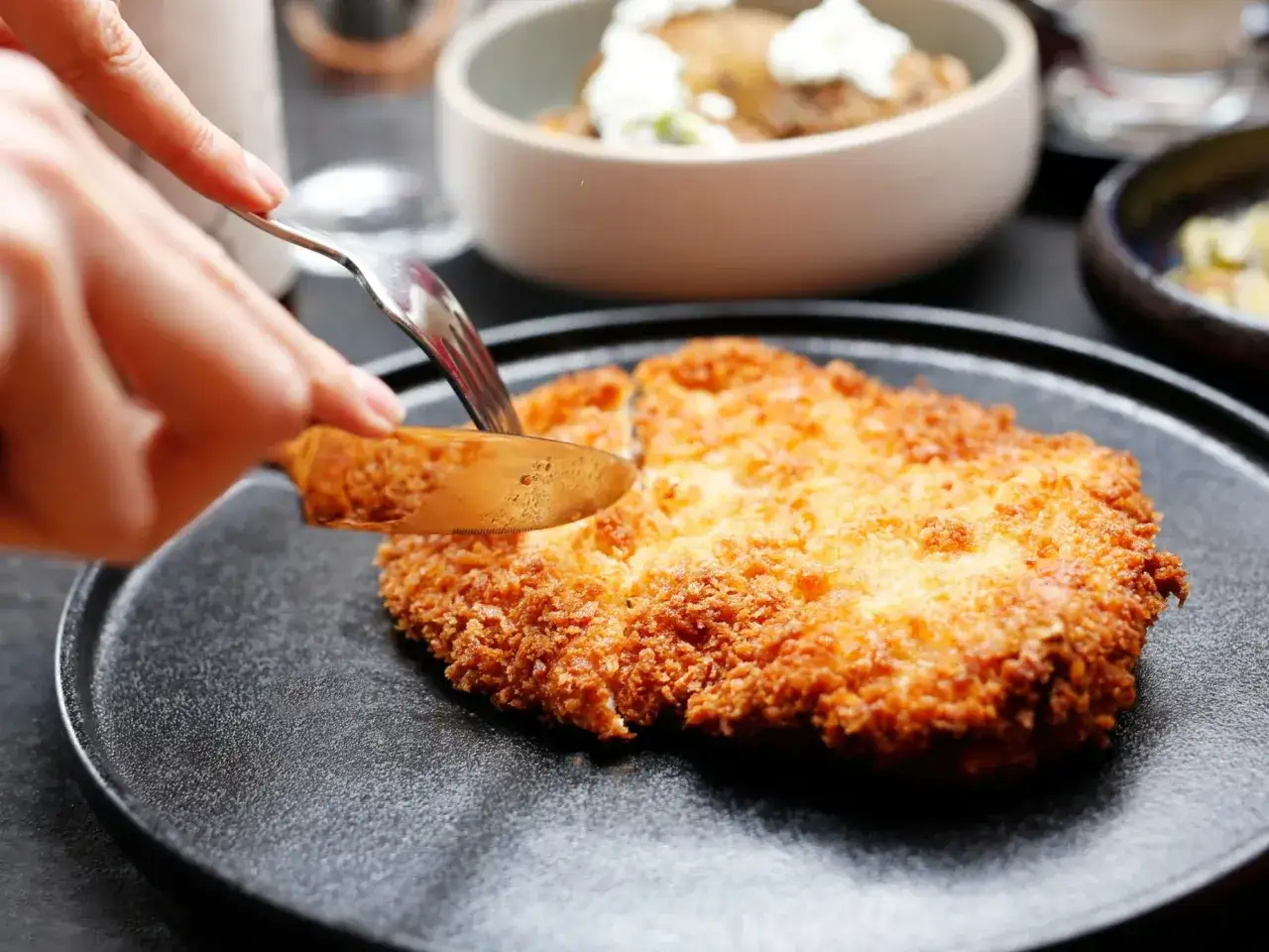 Złocisty kotlet schabowy na czarnym talerzu, kroimy go widelcem i nożem. Idealny do podania, gdy zastanawiasz się, jak długo smażyć kotlety schabowe.