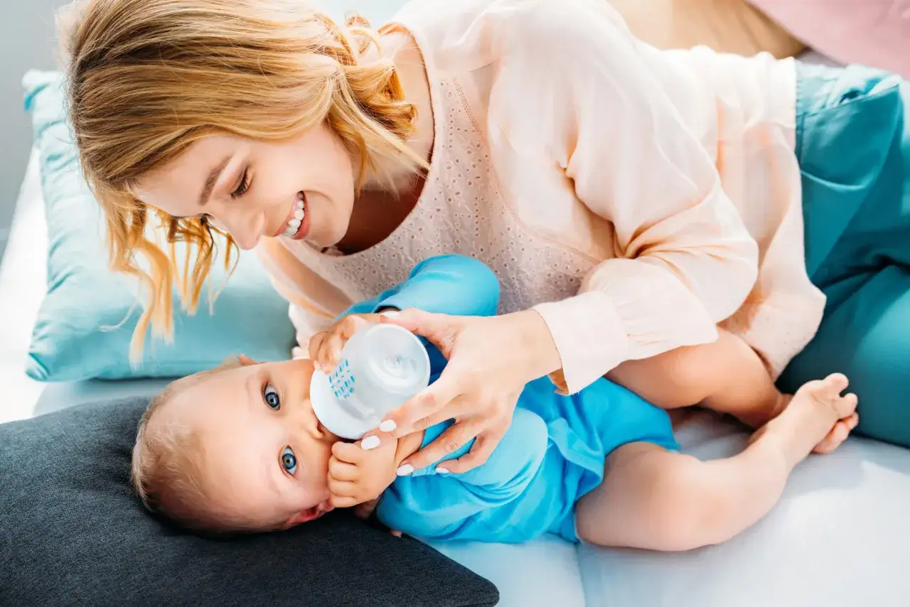 Uśmiechnięta mama karmi butelką niemowlę. To może być zdrowe mleko roślinne dla niemowlaka, które zapewnia mu wszystko, co potrzebne do rozwoju.