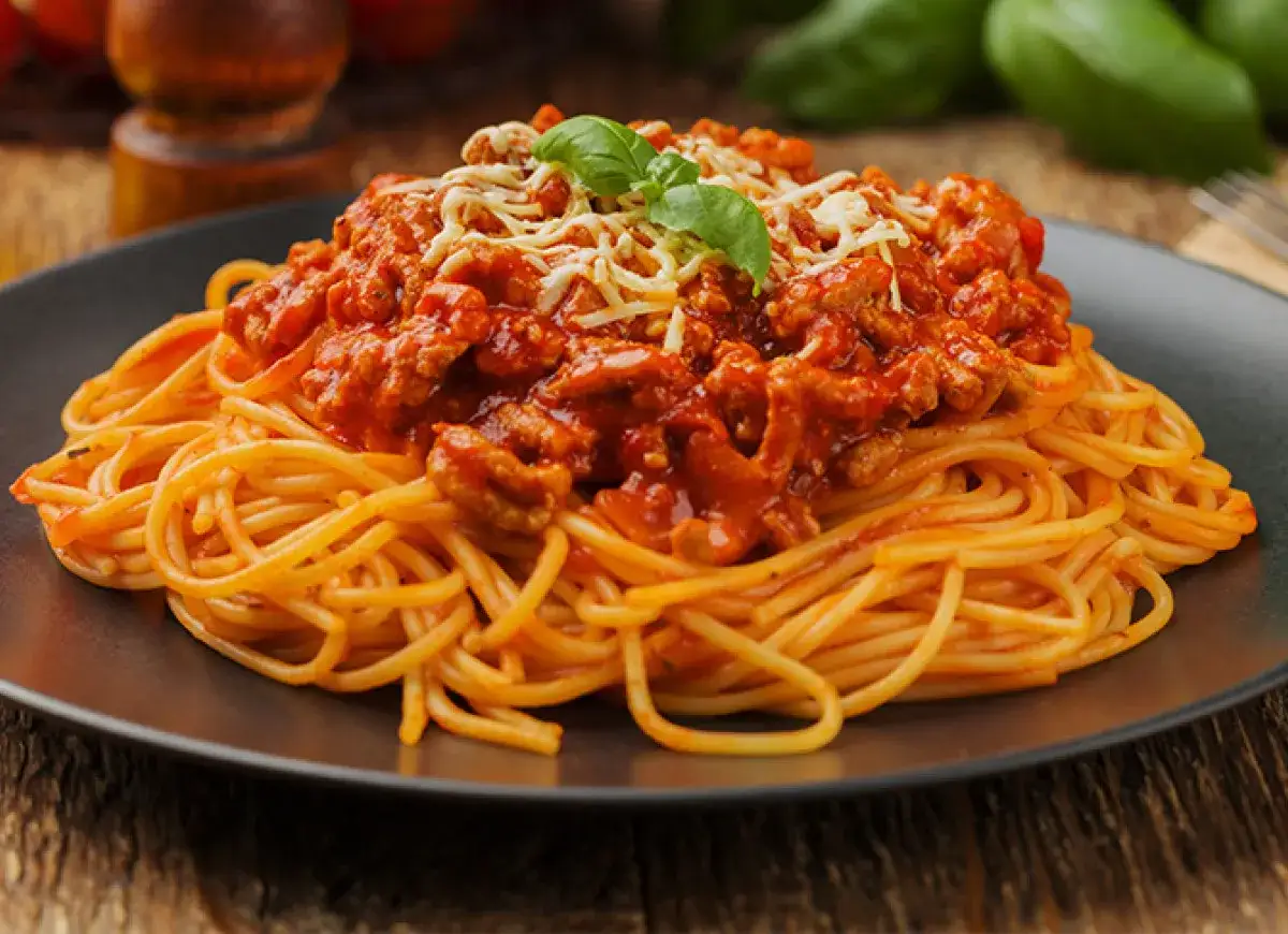 Porcja spaghetti bolognese z mięsem mielonym i sosem pomidorowym, posypana serem. Czy spaghetti bolognese jest zdrowe? Zależy od składników!