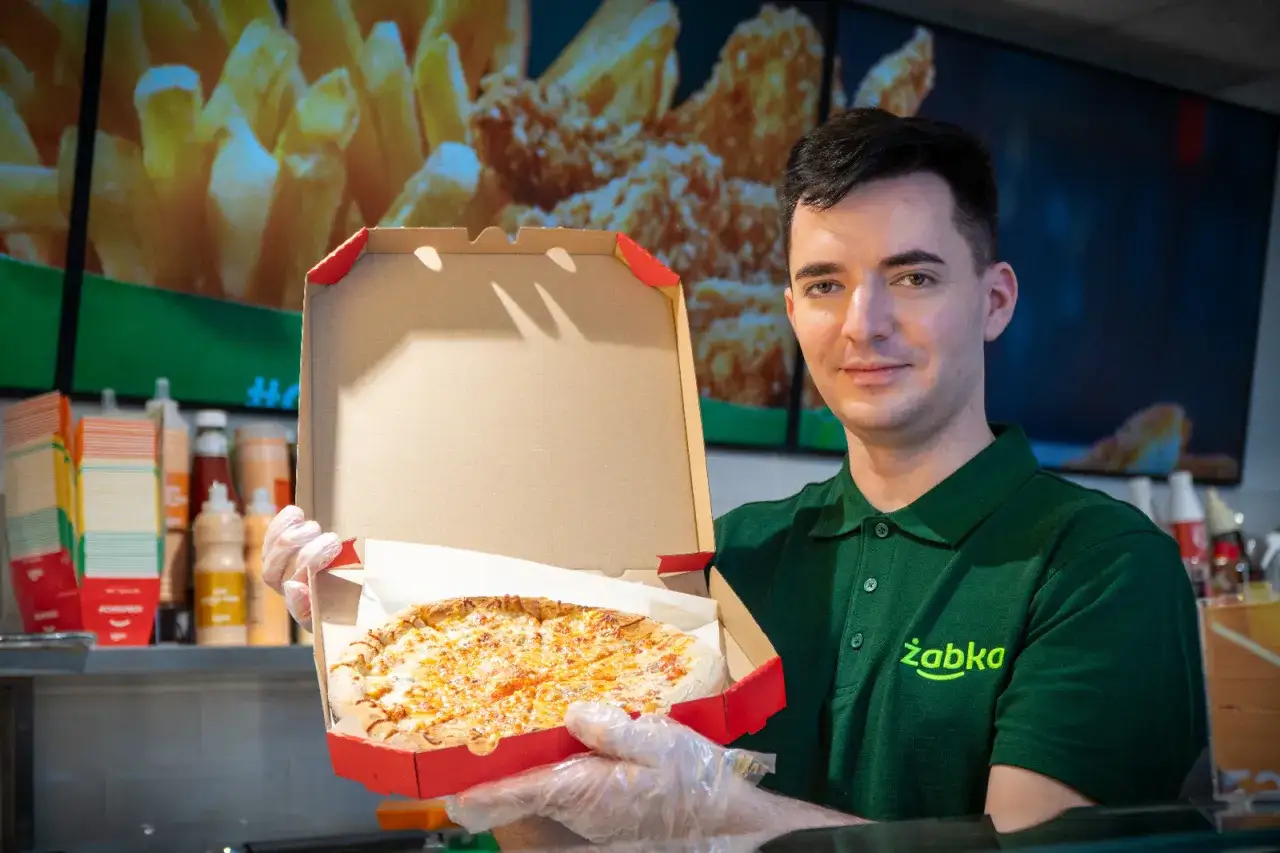 Pracownik Żabki prezentuje pizzę. Dowiedz się, ile kosztuje pizza w Żabce i jakie są jej składniki.