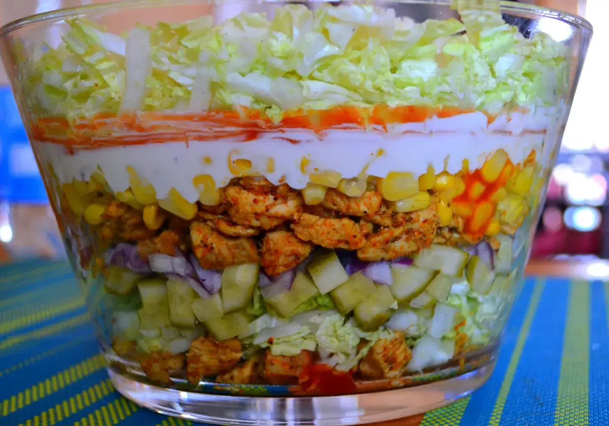 Warstwowa sałatka gyros w szklanej misie. Zastanawiasz się, ile może stać sałatka gyros w lodówce? Ta wygląda apetycznie!