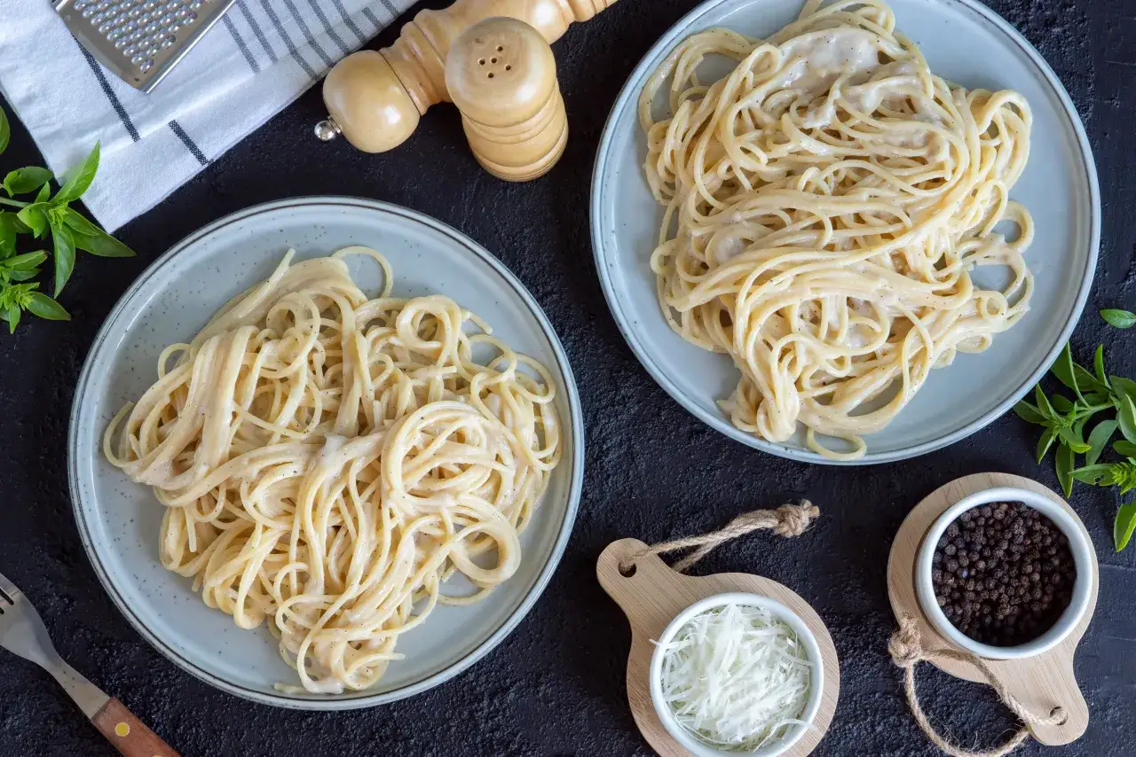Dwa talerze spaghetti carbonara, miseczka startego sera, ziarna pieprzu i przyprawy. Idealne, gdy zastąpić ser pecorino.