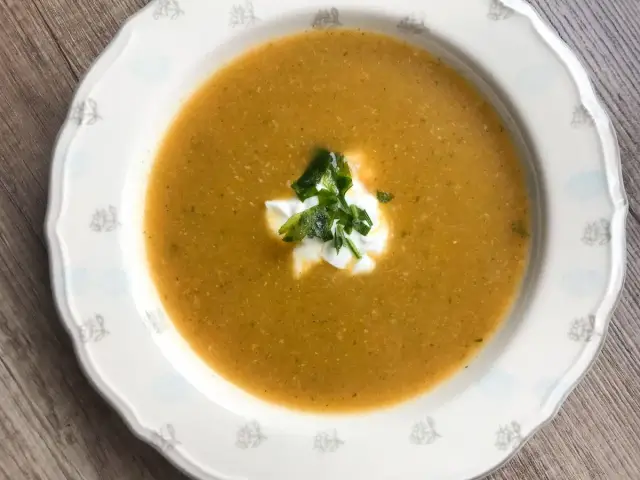 Aksamitna zupa na bazie rosołu, udekorowana kleksem śmietany i świeżą natką pietruszki, podana w ozdobnej miseczce.